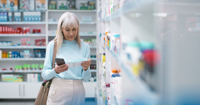 Box, medicine and phone with woman in pharmacy to search for chronic or prescription medication. Healthcare, pharmaceuticals and reading with mature customer in drugstore for supplement choice